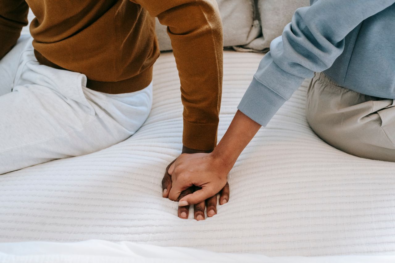 heros-img Crop faceless African American couple sitting on bed back to back and holding hands